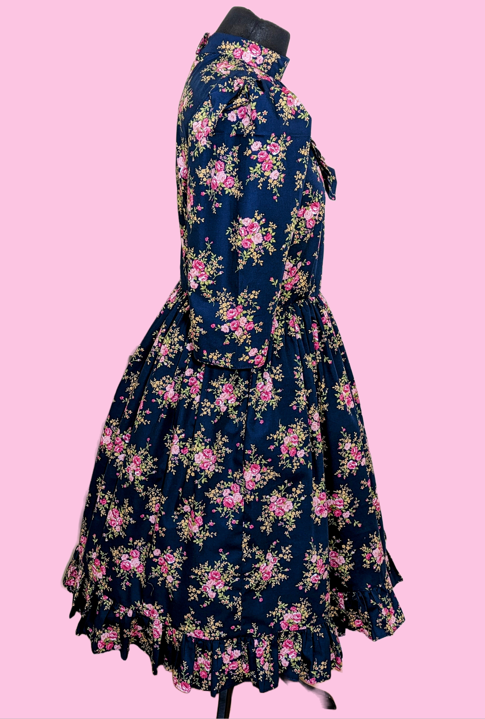 This Blue Floral Prairie Dress features beautiful pink flowers on a navy cotton fabric, with a 1970s-style vintage dress and Edwardian-inspired bodice. A timeless and elegant tea-length dress reminiscent of the iconic Little House on the Prairie