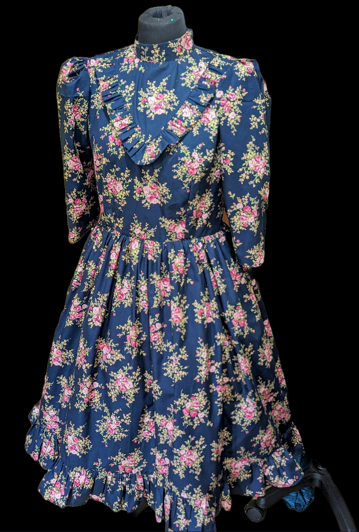 This Blue Floral Prairie Dress features beautiful pink flowers on a navy cotton fabric, with a 1970s-style vintage dress and Edwardian-inspired bodice. A timeless and elegant tea-length dress reminiscent of the iconic Little House on the Prairie