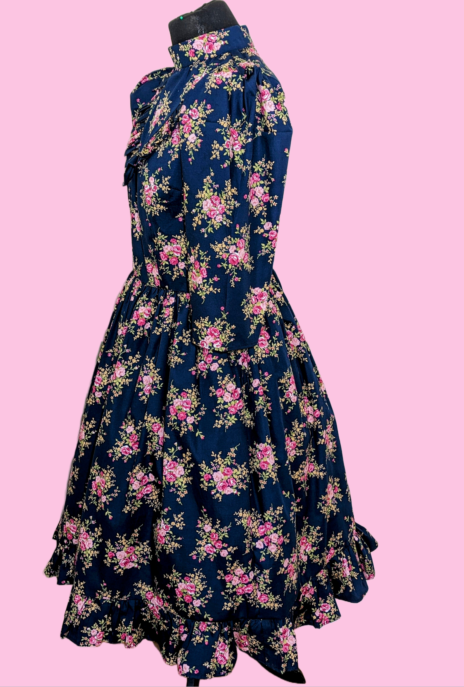 This Blue Floral Prairie Dress features beautiful pink flowers on a navy cotton fabric, with a 1970s-style vintage dress and Edwardian-inspired bodice. A timeless and elegant tea-length dress reminiscent of the iconic Little House on the Prairie