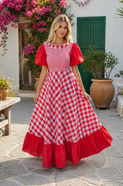 Woman wearing a red and white checkered dress in an outdoor setting with plants and a building.