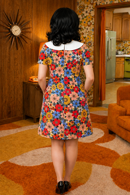 Person wearing a colorful floral dress in a retro-style room with patterned wallpaper and furniture.