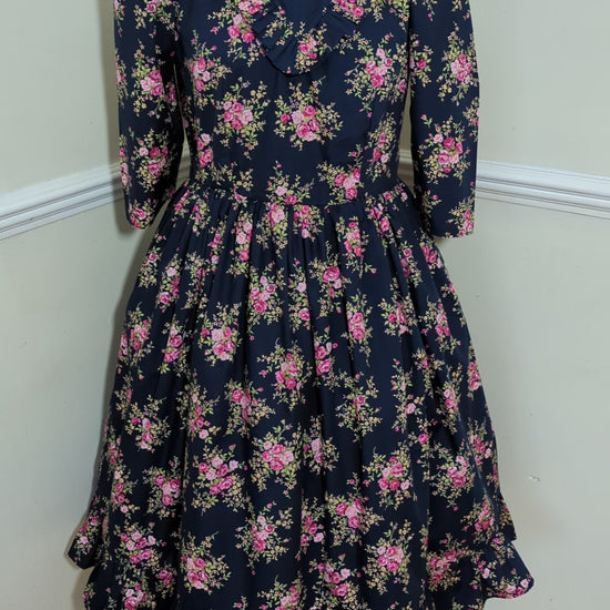 This Blue Floral Prairie Dress features beautiful pink flowers on a navy cotton fabric, with a 1970s-style vintage dress and Edwardian-inspired bodice. A timeless and elegant tea-length dress reminiscent of the iconic Little House on the Prairie