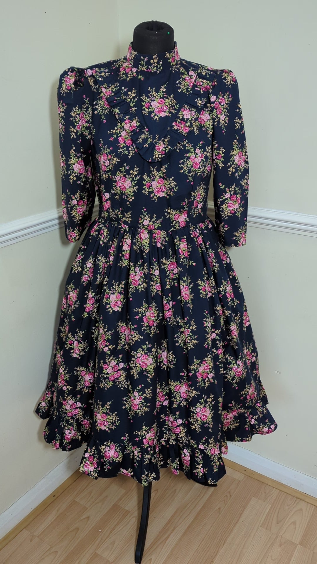 This Blue Floral Prairie Dress features beautiful pink flowers on a navy cotton fabric, with a 1970s-style vintage dress and Edwardian-inspired bodice. A timeless and elegant tea-length dress reminiscent of the iconic Little House on the Prairie